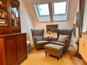 A cozy loft bedroom with a skylight, a wooden cabinet, two armchairs, a small table, and a radiator. - Wohnung Lotte Petersen - Willi Ohler Haus (Worpswede)