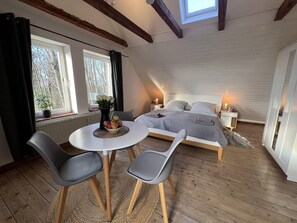 A cozy bedroom with a bed, bedside tables, and a window. There is a small table with chairs in the corner. - Wohnung Atelier - Willi Ohler Haus (Worpswede)