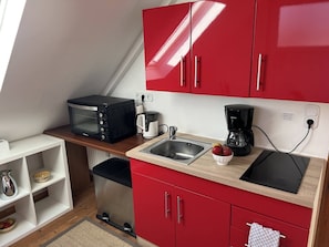 Una cocina compacta con armarios rojos, un microondas, una cafetera y un lavabo.