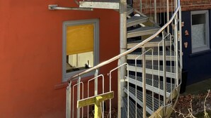 Una escala espiraltra adossada a un edifici amb façana vermella i secció blava fosca.