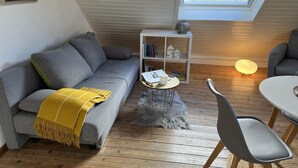 Un acogedor espacio tipo loft con un sofá gris, una mesita blanca, una estantería y un tragaluz.