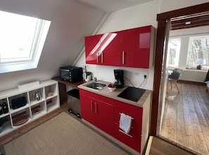Una cocina compacta con armarios rojos, un microondas, una cafetera y un lavabo.