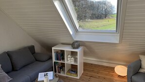 Un dormitori tipus loft acollidor amb sostre inclinat, un fanal i un sofà gris, una biblioteca blanca i una taula rodona de fusta.