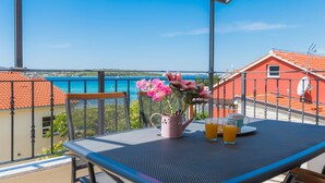 A balcony with a table set for two, a pink flower vase, and a view of the sea and buildings. - Gorgeous apartment in Srima with WiFi (Srima)