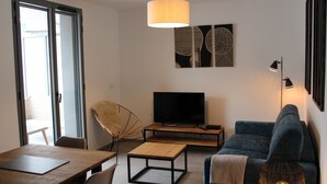 A modern living room with a sofa, a coffee table, a TV, and a dining area with chairs and a table. - Beautiful apartment facing Prorel. In the town center. (Briançon)