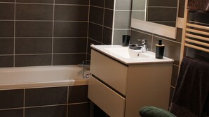 A modern bathroom with a bathtub, a sink, a toilet, and a mirror. - Beautiful apartment facing Prorel. In the town center. (Briançon)