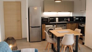 A modern kitchen with a refrigerator, microwave, and dishwasher. There is a dining table with chairs and a hanging light fixture. - Beautiful apartment facing Prorel. In the town center. (Briançon)