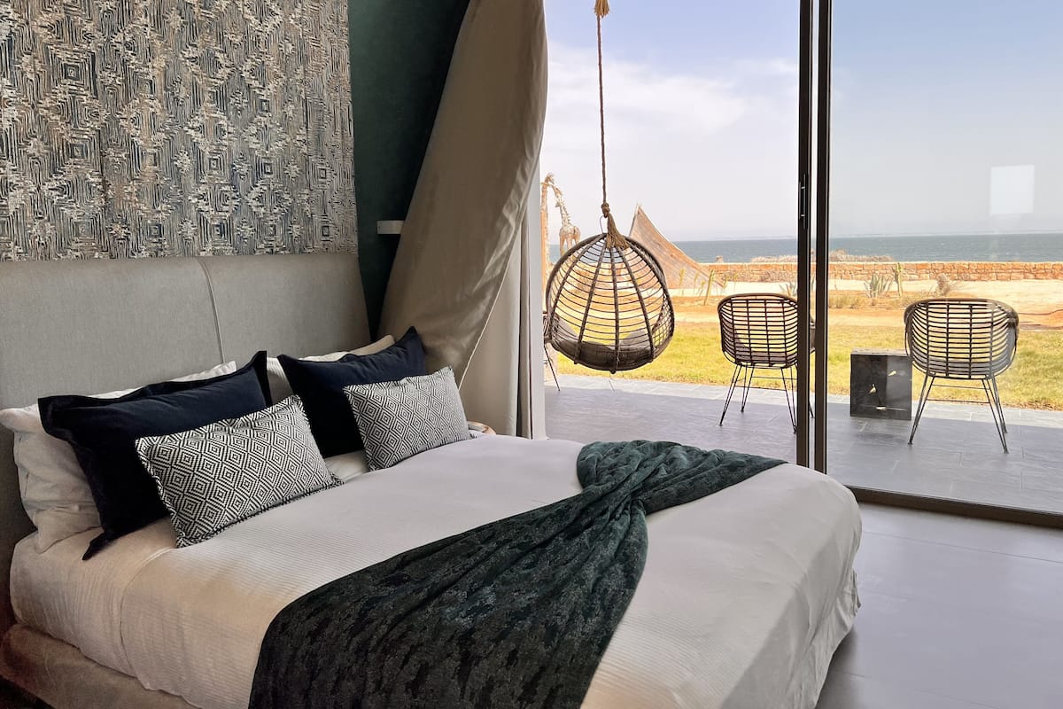 Une chambre avec un grand lit, un fauteuil suspendu et une vue sur la plage.