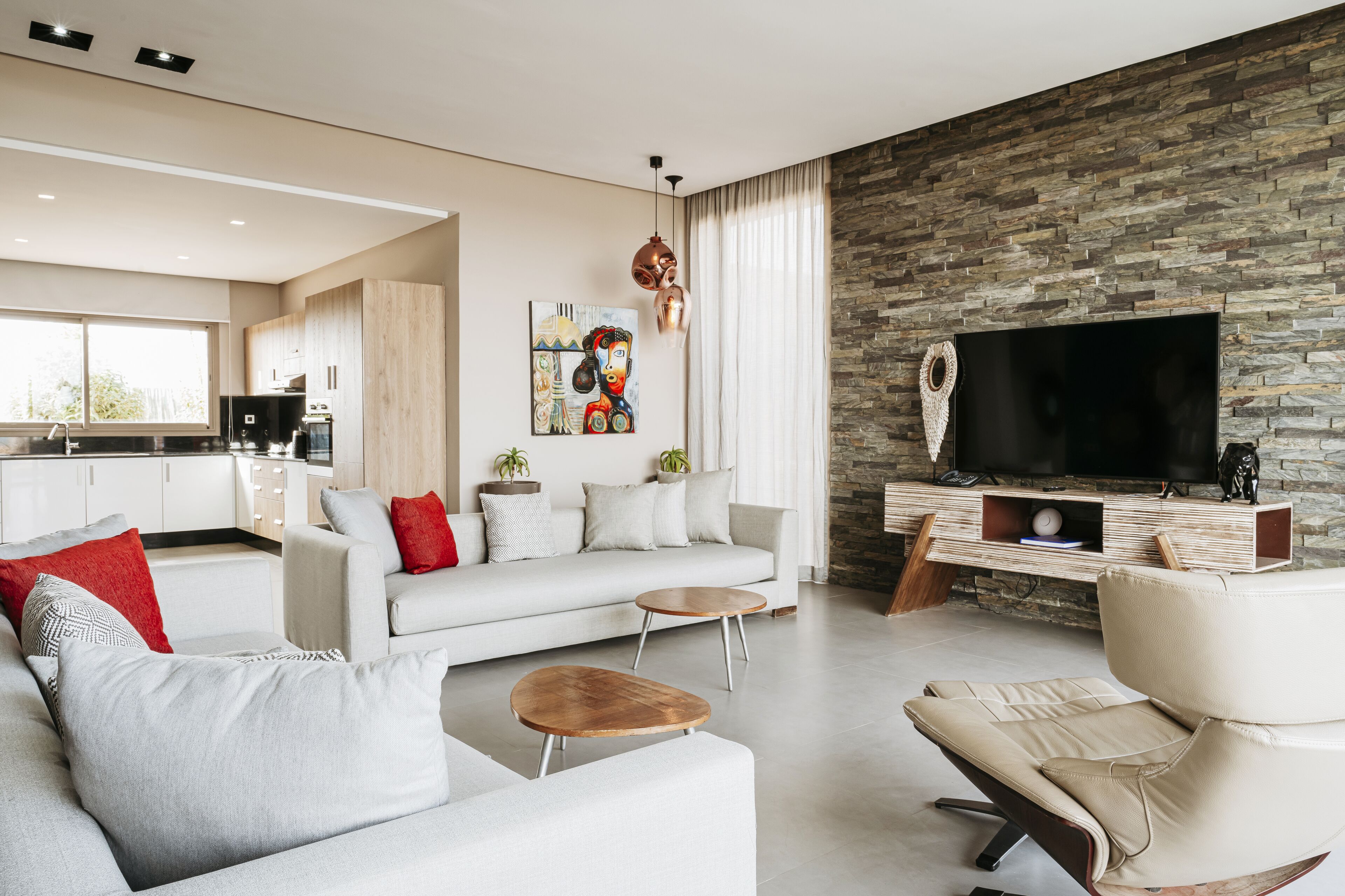 Una sala de estar moderna con una pared de acento de piedra, un televisor de pantalla plana, un sofá, una mesa de centro y un comedor al fondo.
