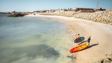 Una playa con agua cristalina, costa rocosa y edificios al fondo.