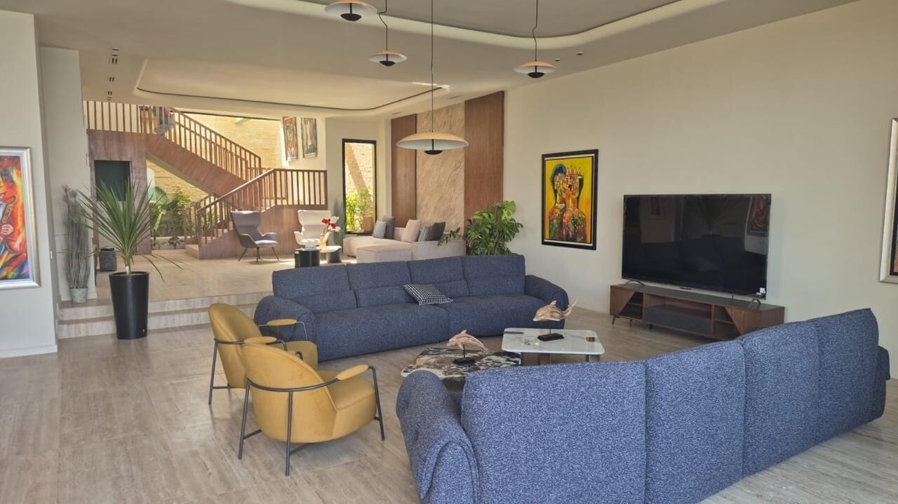 A modern living room with a large blue sectional sofa, a yellow armchair, and a flat-screen TV.