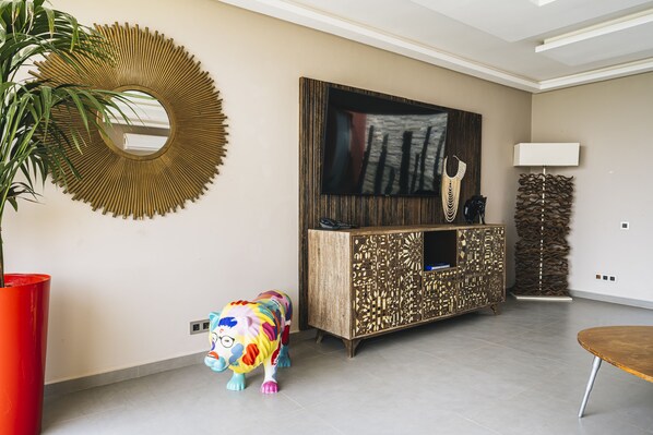 A modern living room with a large mirror, a television, a decorative cabinet, a lamp, and a colorful toy horse.
