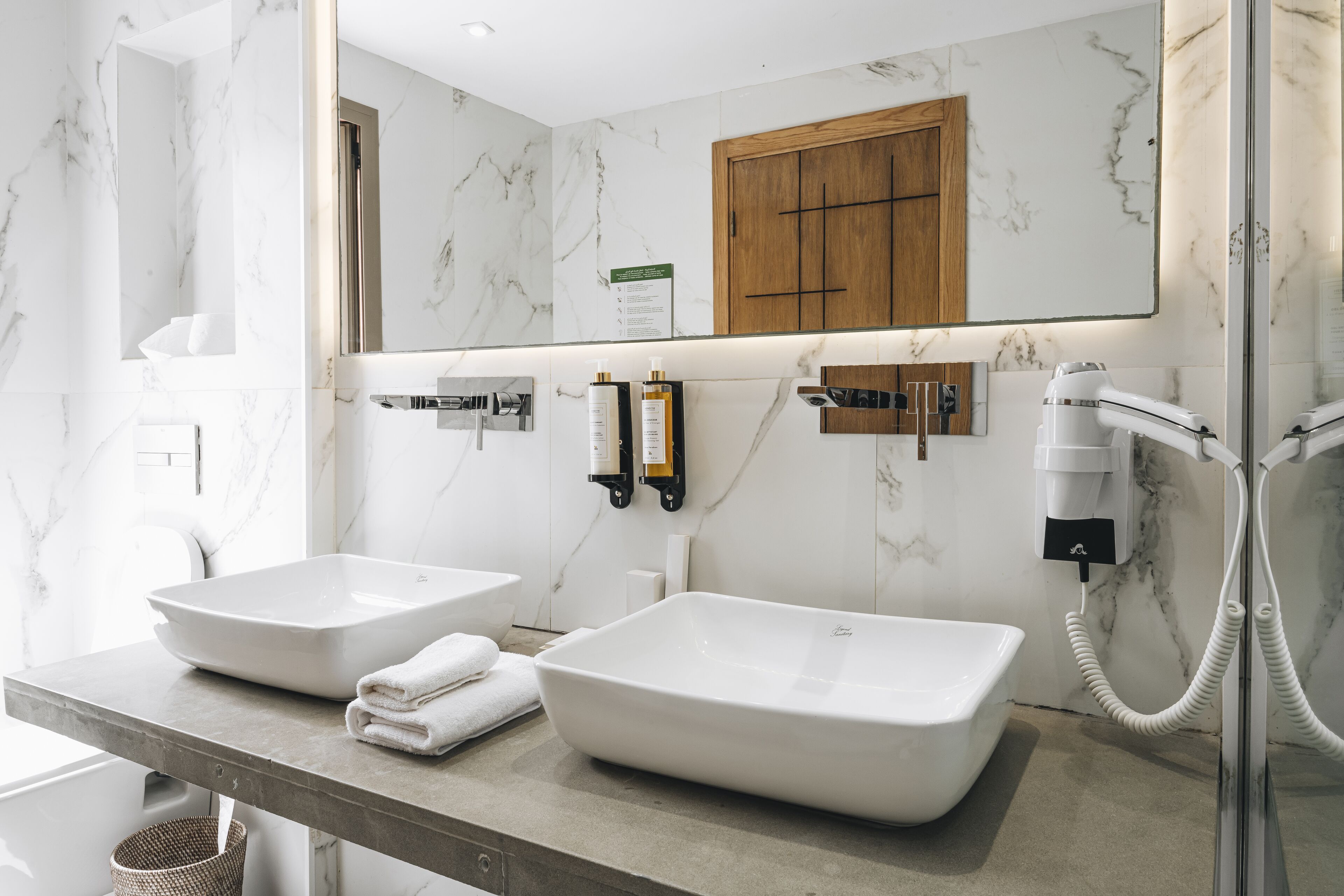A modern bathroom with two large sinks, a wooden cabinet, a mirror, and a handheld showerhead.