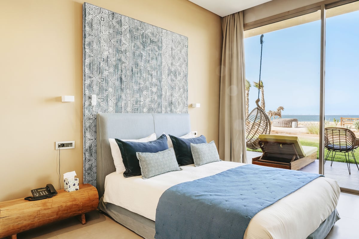 Une chambre d’hôtel moderne dotée d’un grand lit, offrant une vue sur la plage et comprenant un balcon avec mobilier d’extérieur.