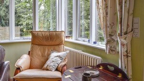 Une pièce avec un fauteuil en cuir, une petite table sur laquelle se trouve une tasse, et une fenêtre avec des rideaux.
