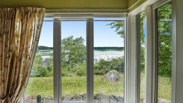 Une pièce dotée d’une grande fenêtre donnant sur un lac, d’un rideau et d’un rebord de fenêtre sur lequel sont posés des verres.
