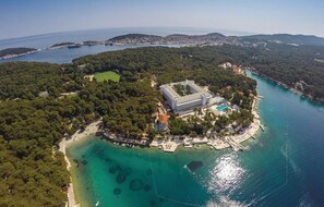 Eine Luftaufnahme einer Küstenimmobilie mit einem zentralen Gebäude, umgeben von üppigem Grün und klarem türkisblauem Wasser.