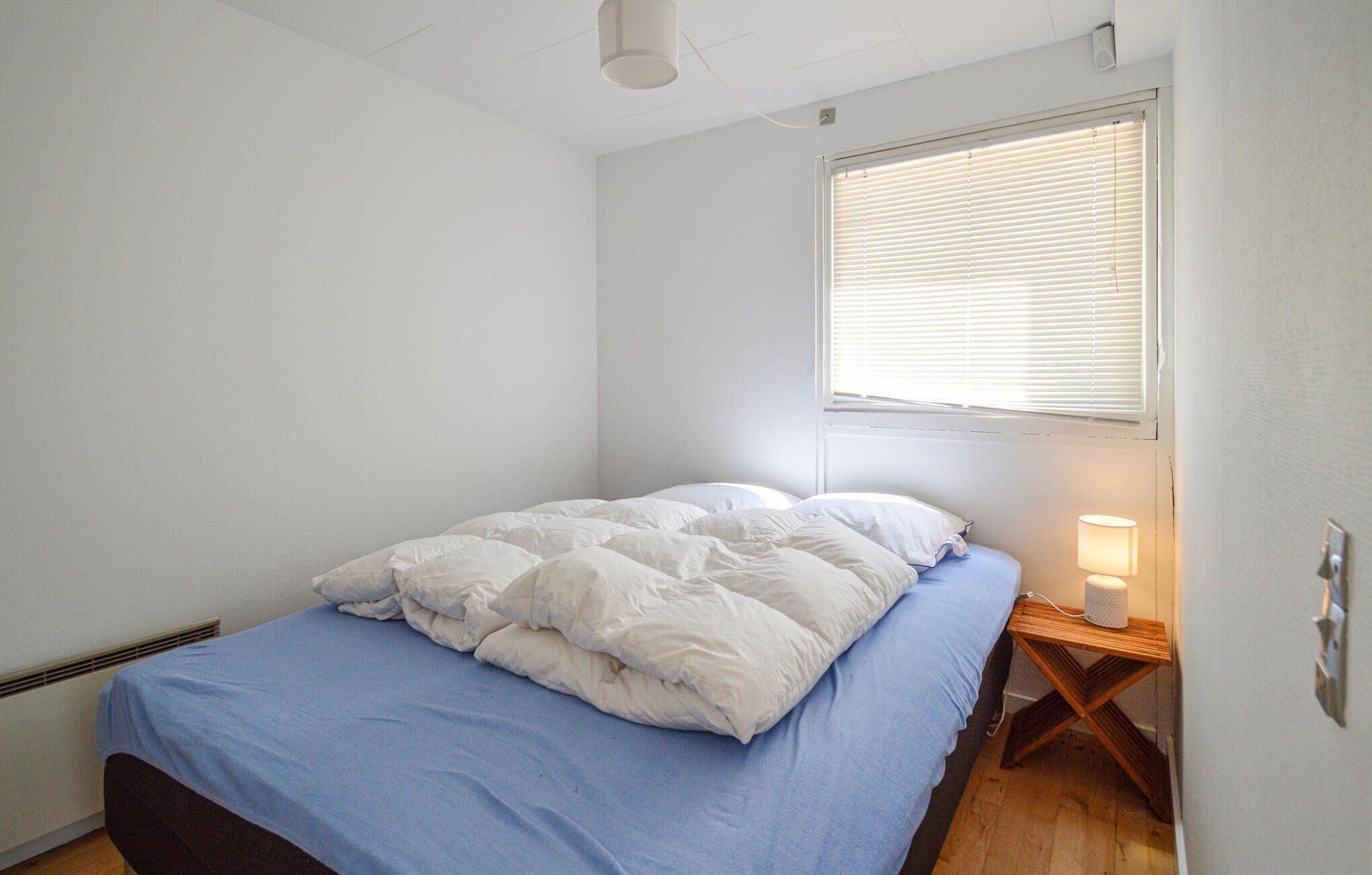 Ein Schlafzimmer mit einem Einzelbett, einem Nachttisch mit Lampe und einem Fenster mit Jalousien.
