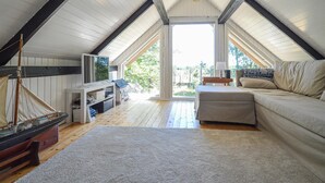 A cozy attic bedroom with a wooden ceiling, a large window, a sailboat model, a sofa, and a small table. - Lovely home in Væggerløse with kitchen (Væggerløse)