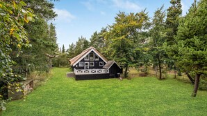 A small, black and white cabin with a thatched roof, surrounded by a well-maintained lawn and trees. - Lovely home in Væggerløse with kitchen (Væggerløse)