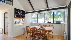 A dining area with a wooden table and chairs, a kitchen with white cabinets, and a large window with a view of trees. - Lovely home in Væggerløse with kitchen (Væggerløse)