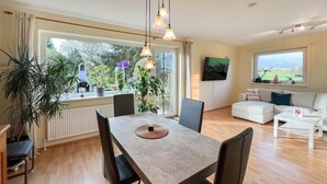 Ein modernes Wohnzimmer mit Essbereich, großen Fenstern und Blick ins Grüne.