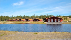 Una hilera de cabañas rojas, con un lago al frente y un bosque de fondo.