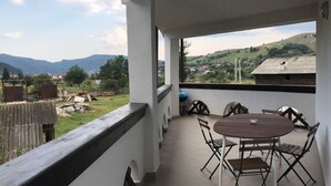 Un balcon avec une table et des chaises, donnant sur un paysage rural avec des collines et des maisons.
