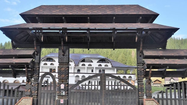 Une porte traditionnelle en bois, surmontée d’un toit en métal, qui mène à un bâtiment à la façade blanche et doté de nombreuses fenêtres.