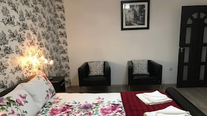 Une chambre d’hôtel avec un lit, deux chaises, un plaid rouge et un tableau encadré au mur.
