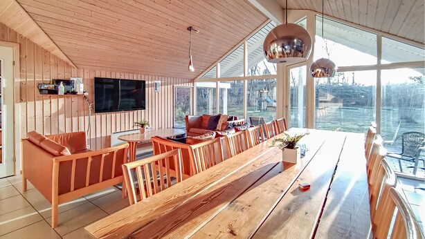 Amplia sala de estar con una gran mesa de madera, asientos cómodos, un televisor de pantalla plana y ventanas amplias que ofrecen vistas al exterior.