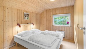 Habitación con paneles de madera, una cama, una ventana con vistas a la vegetación y una estantería con vasos y una fotografía.