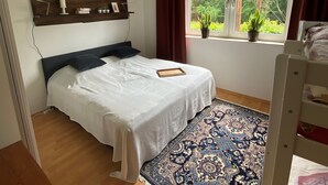 A bedroom with a bed, a wooden headboard, a window with curtains, and a patterned rug. - beautiful, very quiet apartment with terrace  (Winterberg)