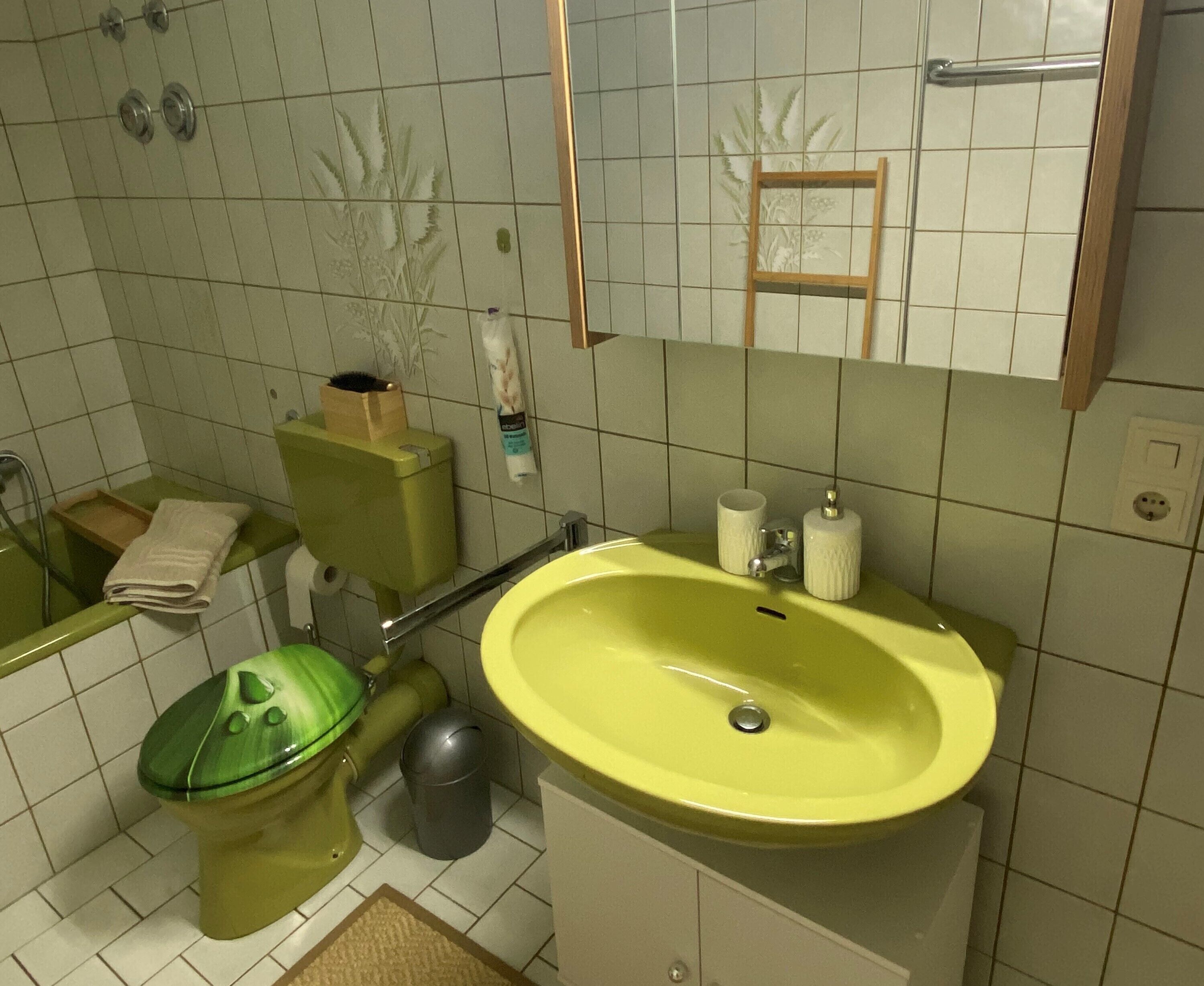 A bathroom with a green toilet, a yellow sink, and a mirror above the sink.