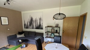 A living room with a sofa, a dining table with chairs, a bookshelf, and a painting on the wall. - beautiful, very quiet apartment with terrace  (Winterberg)
