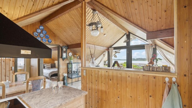 Een houten blokhut van binnen, met een keukenhoek, een eethoek en een slaapkamer.