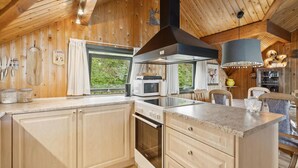 Een moderne keuken met houten wanden, een groot eiland en een eetgedeelte met uitzicht op groen.