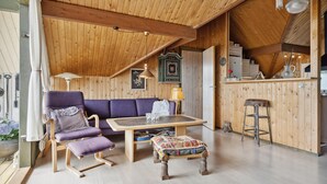 Een gezellig interieur van een blokhut met een houten plafond, een paarse bank, een houten tafel en een klein krukje.