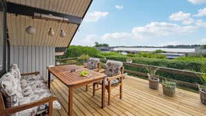Een houten terras met tafel en stoelen, met uitzicht op water en groen.