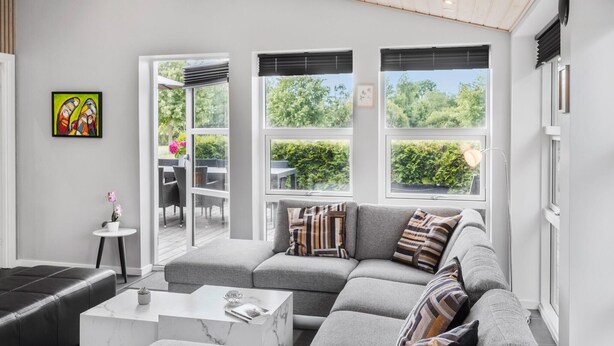 Ein modernes Wohnzimmer mit einer grauen Couch, einem weißen Couchtisch und Blick auf einen Garten durch große Fenster.