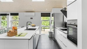 Eine moderne Küche mit Kochinsel, Edelstahlgeräten und großen Fenstern.