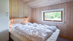 Un dormitorio con cama, paredes de madera, una ventana y una mesita de noche con lámpara.