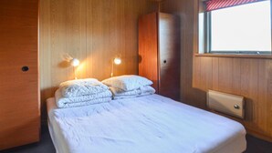 A neatly made bed with white linens, two bedside lamps, and a window with a red and white striped curtain.