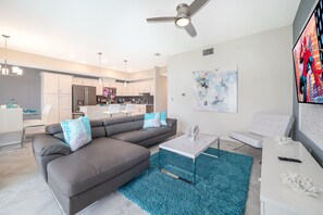 Un salon moderne avec un canapé d’angle, une table basse blanche et un tapis bleu.