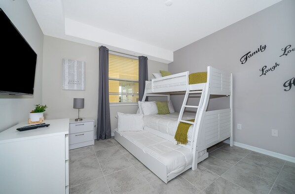 A bedroom with a bunk bed, a desk with a plant, a TV, and a window with curtains.