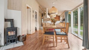 A spacious living room with a wood-burning stove, a dining area with a large table and chairs, and a view of the outdoors through large windows. - Stunning home in Fjerritslev with WiFi (Fjerritslev)