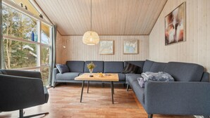 A modern living room with a grey sectional sofa, a wooden coffee table, and a black armchair. There are two framed artworks on the wall and a large window offering a view of trees and a house. - Stunning home in Fjerritslev with WiFi (Fjerritslev)