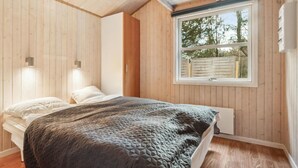 A bedroom with a bed, two bedside lamps, a window with a view of trees, and wooden walls. - Stunning home in Fjerritslev with WiFi (Fjerritslev)