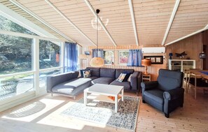 Moderni olohuone, jossa on sohva, nojatuoli, sohvapöytä ja suuret ikkunat.