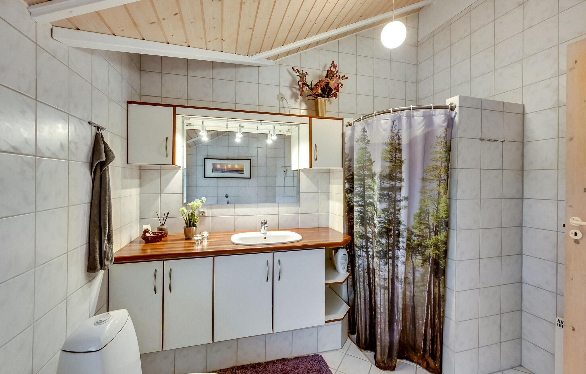 Ein modernes Badezimmer mit einem Holzausleger, weißen Schränken, einem Waschbecken und einem Duschvorhang mit Waldmotiv.